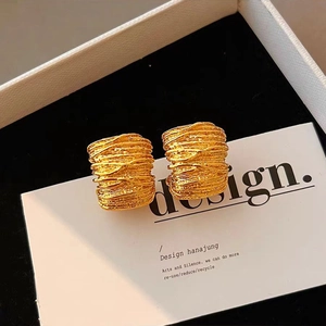 Detailed close-up of golden cylindrical earrings with fine textured wire winding on white card