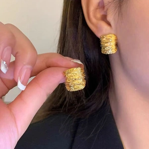 Close-up of golden C-shaped stud earrings with unique metal wire winding design