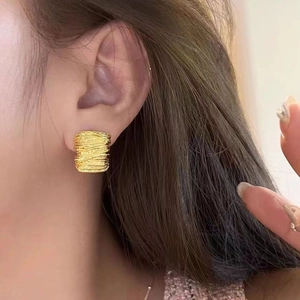Detail shot of golden C-shaped stud earrings with intricate pleated metal texture