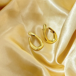 Macro di orecchini a U geometrici placcati oro su un elegante tessuto di seta dorata