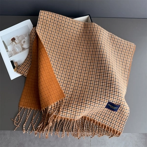 Détail d'une écharpe à carreaux orange en cachemire avec franges et étiquette de marque