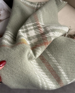 Close-up of green plaid knit scarf showing soft texture and delicate tassel fringe details