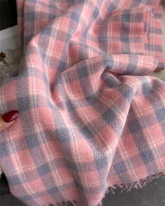 Gros plan sur l'écharpe à carreaux rose et gris montrant le tissage doux et franges