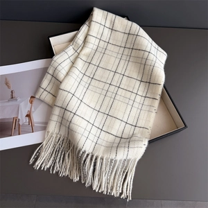 Detail view of ivory plaid cashmere scarf with soft fringes on a dark tray