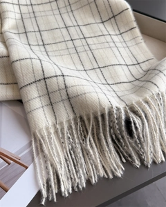 Close-up of elegant cream plaid scarf showing soft fabric texture and tassel fringe details