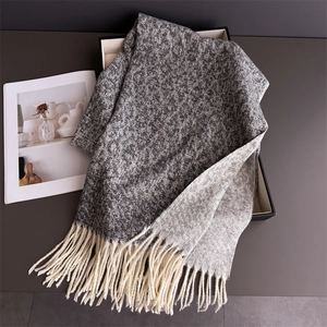 Detailed view of grey mixed knit scarf with soft cream-colored fringe on a gift box