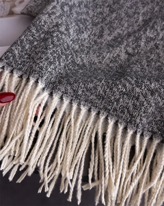 Close-up of thick knit shawl fabric with long cream tassels and grey textured weave