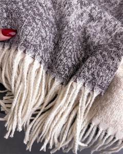 Detailed view of grey and white knit scarf texture featuring soft cream fringe tassels