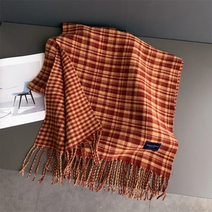 Detail view of red and yellow plaid scarf featuring soft cashmere-like fringe and woven label