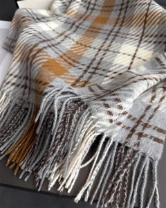 Detail of plaid scarf featuring gray and caramel checkered pattern with soft fringe edges