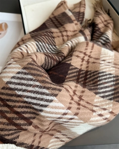 Detailed close-up of plaid cashmere scarf texture with tassels in a premium gift box
