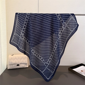 Navy blue polka dot square silk scarf with cross patterns hanging in a minimalist setting