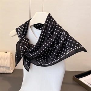 Detailed drape of a black polka dot silk scarf styled on a mannequin with a quilted bag