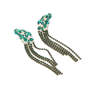 Détail macro de longues boucles d'oreilles pompons en cristaux verts et métal doré