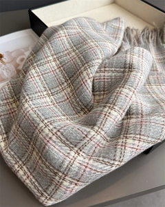 Détail d'une écharpe à carreaux rose et grise avec pompons montrant la texture tissée fine