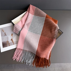 Detailed texture of plaid tassel scarf in pink and orange on a minimalist tray