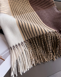 Detail of soft knit texture and fringe tassels on a beige plaid checkered winter scarf