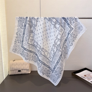 Detail showing blue paisley print on white faux silk scarf with delicate hemmed edge