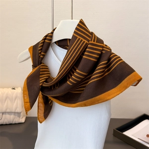 Détail d'un foulard en soie à rayures géométriques noué autour du cou en marron et jaune