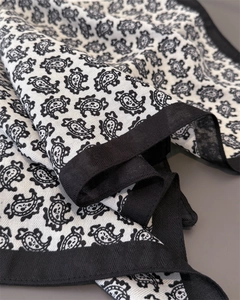 Gros plan du motif paisley noir sur foulard carré crème avec bordure en sergé