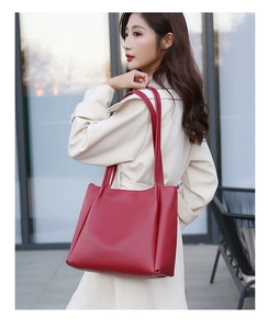 Close-up of a red leather tote bag with matte texture worn over a beige trench coat