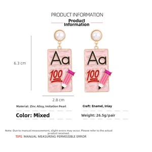Détail de boucles d'oreilles thème école avec crayons roses et motifs A+ 100