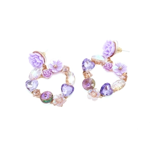 Macro detail of heart-shaped earrings with purple crystal flowers and rose accents