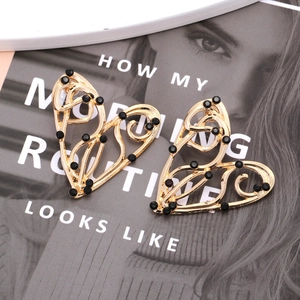 Boucles d'oreilles cœur ajouré vintage dorées avec strass noirs sur fond de magazine