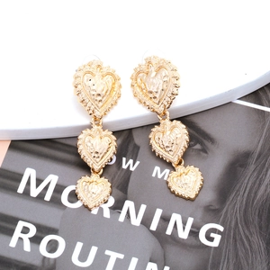 Vintage gold layered heart drop earrings with textured hammered finish on a white pedestal