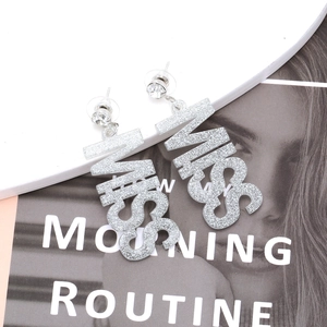 Silver glitter MISS letter drop earrings for women on a stylish magazine background