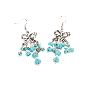 Détail de boucles d'oreilles nœud argenté avec pompons turquoise et perles blanches