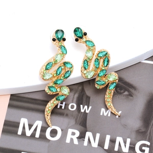 Luxurious gold-plated snake earrings with sparkling green crystals on a fashion magazine