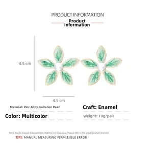 Détail de boucles d'oreilles fleurs en émail vert avec une perle centrale nacrée
