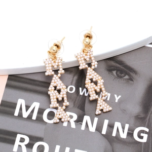 Fashionable gold alloy MAMA letter drop earrings with white inlaid pearls on a white display