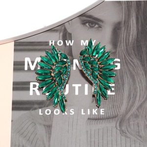 Macro detail of winged earrings with emerald and blue rhinestones on a gold base