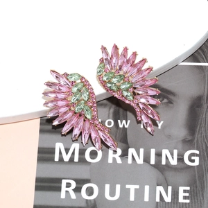 Close-up of glamorous crystal wing earrings with pink and green stones on gold alloy