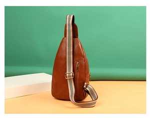 Brown faux leather chest bag with a striped strap and rear zipper pocket on a green backdrop