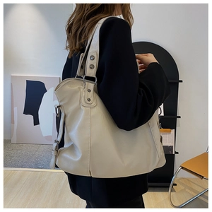 Detail of minimalist cream leather hobo bag featuring metal stud accents on the strap