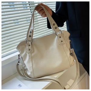 Close-up of beige tote bag with litchi grain texture and metal rivet detail on hand strap