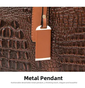 Détail du pendentif en métal doré sur un sac en cuir marron foncé avec motif crocodile
