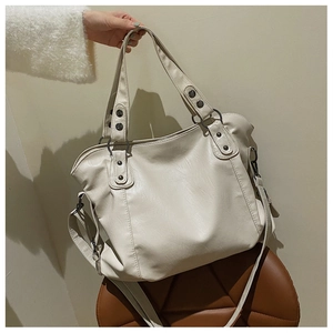 Detail of off-white tote bag with metal studs, leather texture, and detachable strap