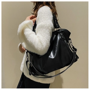 Detail of black leather tote bag with subtle oil-wax texture and crossbody strap