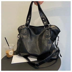 Close-up of black textured faux leather tote bag with silver rivets and metal ring detail