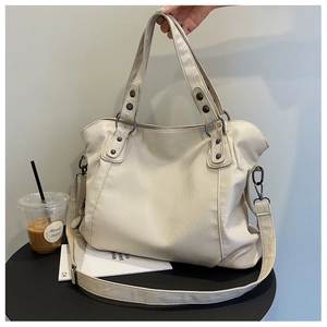 Detail of a cream faux leather tote bag with vintage metal rivets on a black table