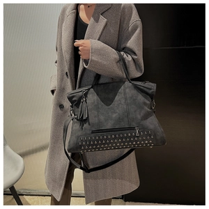 Dark grey hobo bag with stud detailing and fringe tassel worn by a model in grey coat