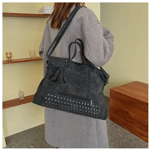 Detail of dark gray matte leather tote with metal rivets and fringe on shoulder
