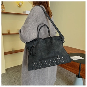 Detail of dark gray matte tote bag with metal rivets, tassels and adjustable shoulder strap