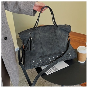 Detail view of large grey tote bag with tassel charms, studs and multiple utility zippers