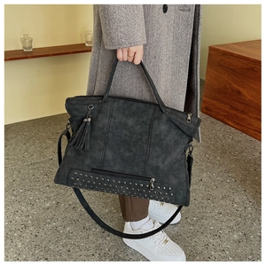 Detail of black faux leather tote bag featuring rivet studs and a stylish tassel charm