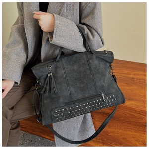 Macro shot of dark grey tote bag featuring metal rivets and elegant fringe detail